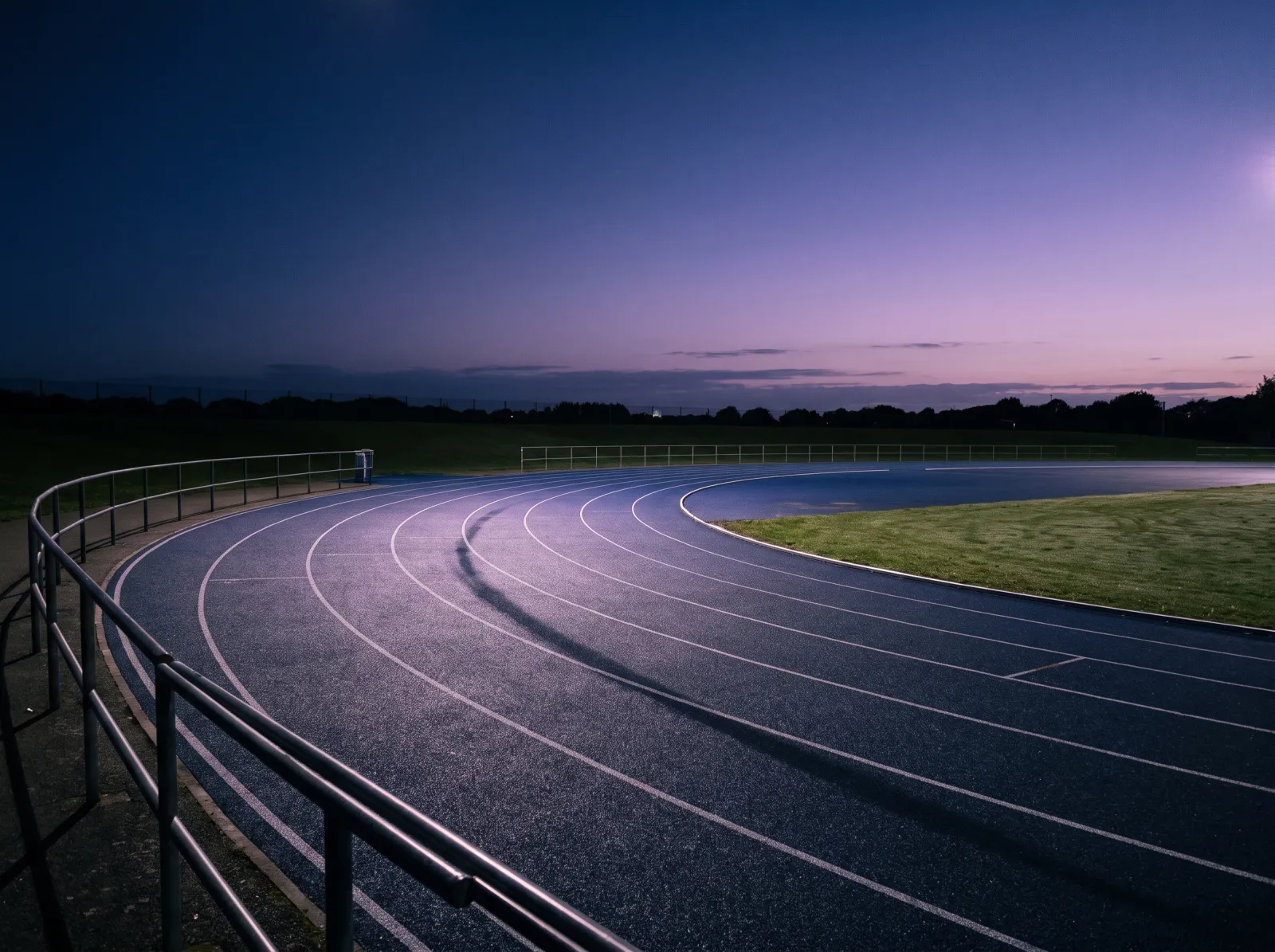 Empty athletics running track at dusk with white lane lines under cinematic lighting